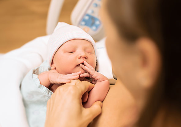 A newborn baby is sleeping in his mother's arms in a hospital bed