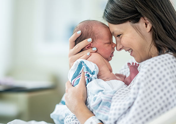 A new mom is happy and holds her newborn baby face to face in the hospital bed