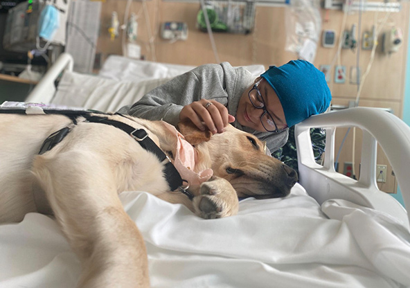 Brisi pets therapy dog Marcus who is laying in her hospital bed with her at CHRISTUS Children's