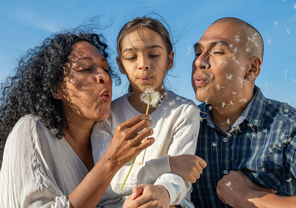Family having fun outside blowing dandelion seeds.