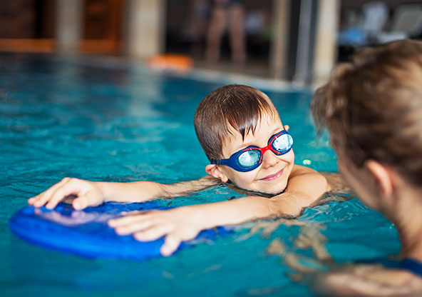 A young boy is using a kickboard in the pool during swim lessons