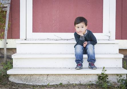 A young child sits on the steps of a shed