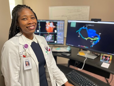 Dr. Esosa Odigie-Okon posing in front of a 3D heart rendering