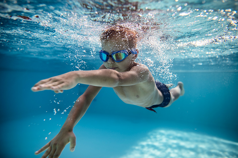 Portrait of little boy swimming underwater in the pool. Sunny summer day.