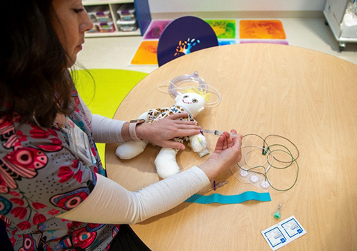 A child life specialist is demonstrating an IV on a doll