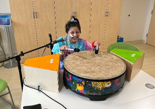 A young girl playing the drums at CHRISTUS Children's through the Music Therapy program